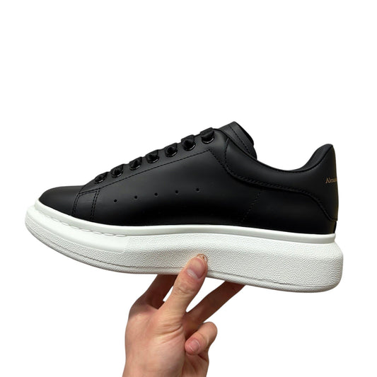 Luxury Chef Alexander McQueen black leather sneakers with white platform sole and gold logo detail.