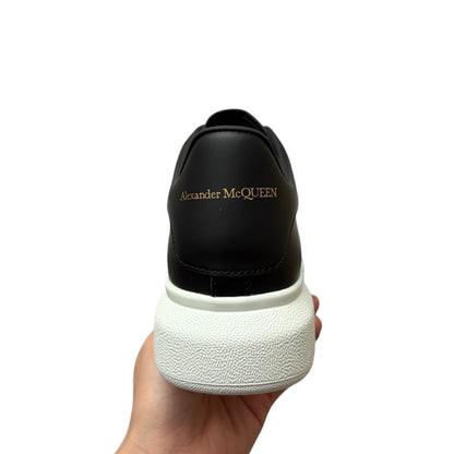 Luxury Chef Alexander McQueen black leather sneakers with white platform sole and gold logo detail.