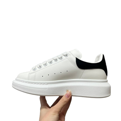 Luxury Chef Alexander McQueen white leather sneakers with black heel tab and thick white sole.