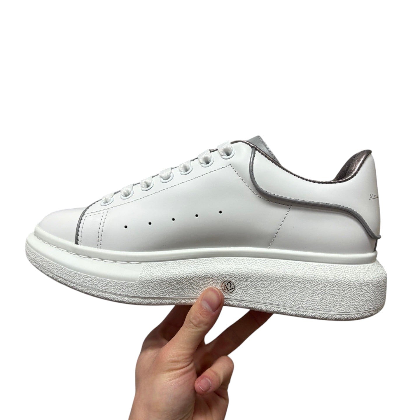 Luxury Chef white leather Alexander McQueen sneakers with silver trim and a chunky sole. Features signature perforations and a metallic heel tab.